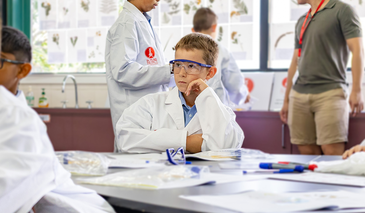 Prep student in uniform with a white lab coat over the top intently listening to the lesson