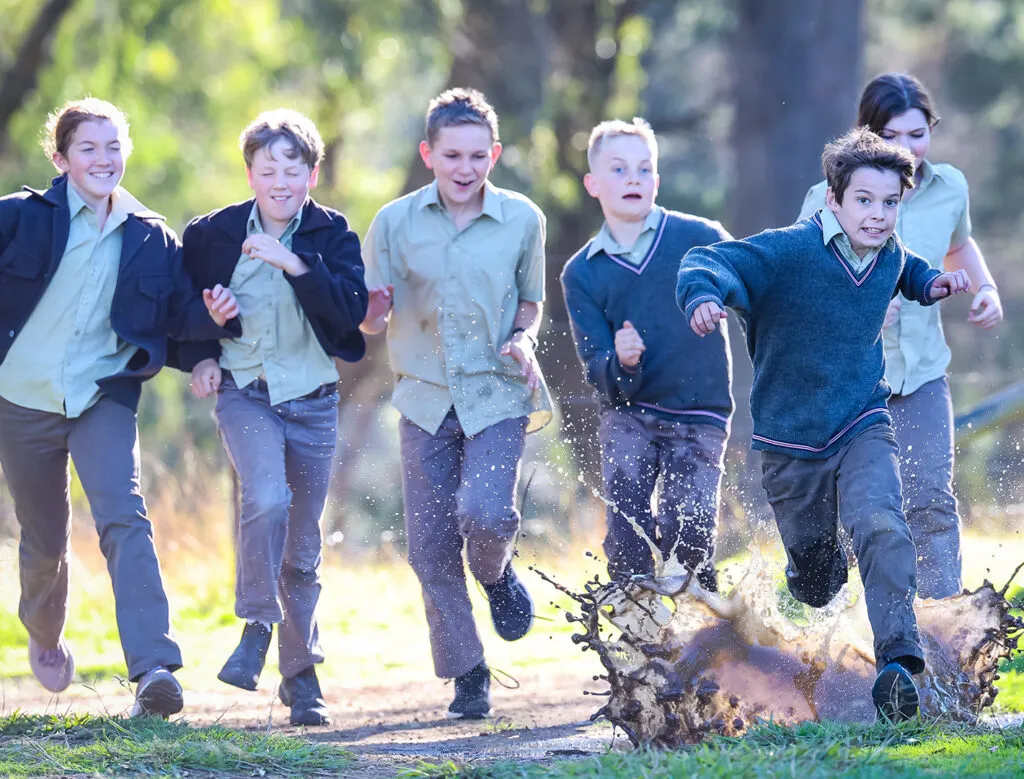 Students in uniform running through mud laughing and smiling